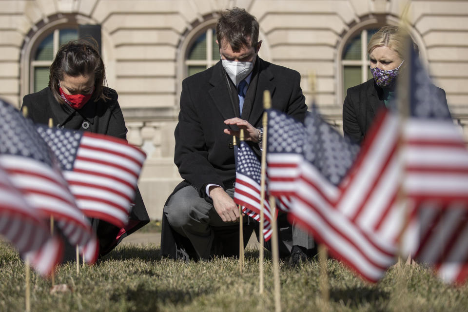 Kentucky Gov. Andy Beshear, with Lt. Gov. Jacqueline Coleman, left, and First Lady Britainy Beshear, places a flag in the ground at the state Capitol in Frankfort, Ky., to memorialize the more than 3,000 Kentuckians who have died from complications from COVID-19 during a ceremony Friday, Jan. 22, 2021. (Ryan C. Hermens/Lexington Herald-Leader via AP)