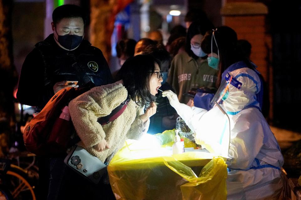 china covid worker in biohazard suit swabs womans mouth covid test with line of people waiting