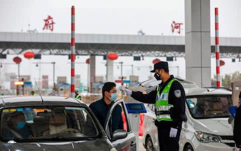 A police officer checks the temperature of a driver at a highway in Wuhan, China - Credit: Getty Images