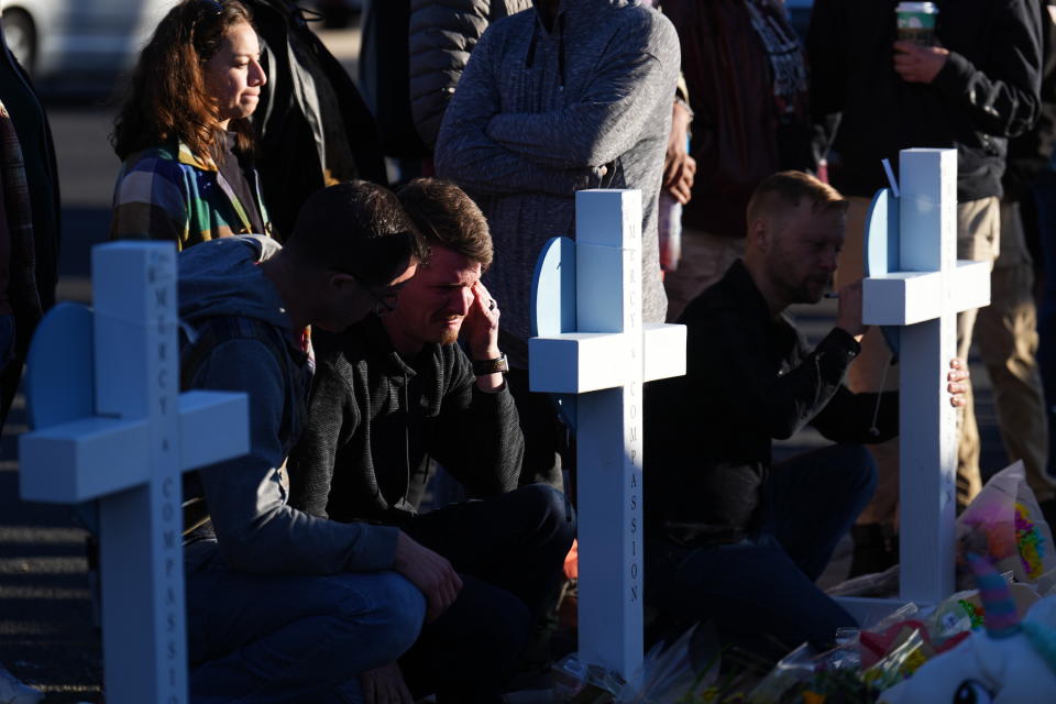 A man cries at a cross set at a makeshift display of bouquets of flowers on a corner near the site of a weekend mass shooting at a gay bar, Monday, Nov. 21, 2022, in Colorado Springs, Colo. (AP Photo/Jack Dempsey)