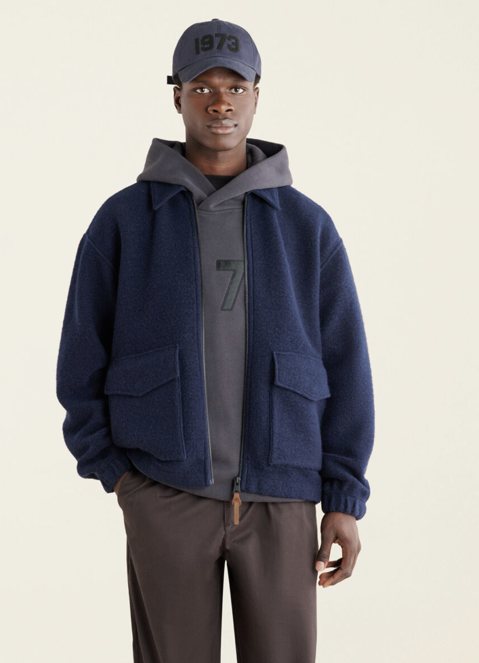 black male model wearing grey hoodie, grey baseball cap and Seymour Jacket in Navy Blazer (Photo via Roots)