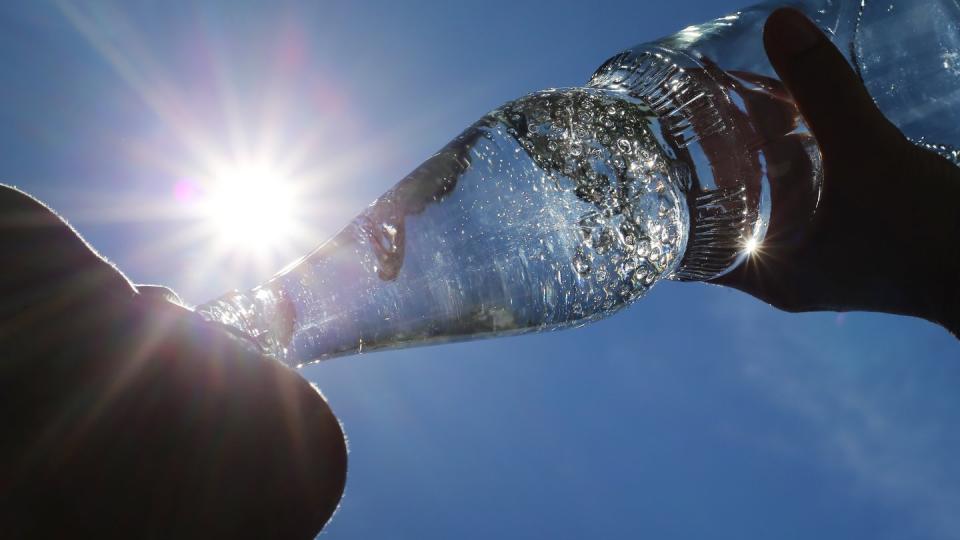 Eine Frau trinkt aus einer Flasche sprudelndes Mineralwasser.