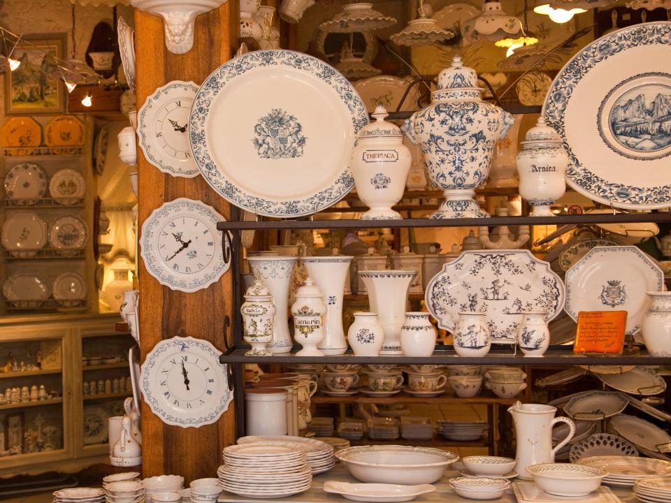 Blue and white china dishes, tea cups, and other tableware on wooden shelf with other dishes on adjacent wooden shelf in background