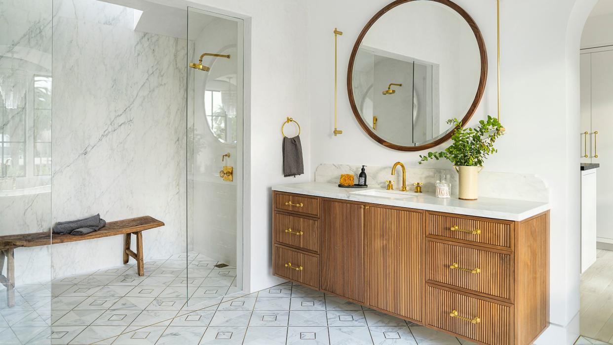  Bathroom with wood vanity and marble top, round mirror and marble shower. 