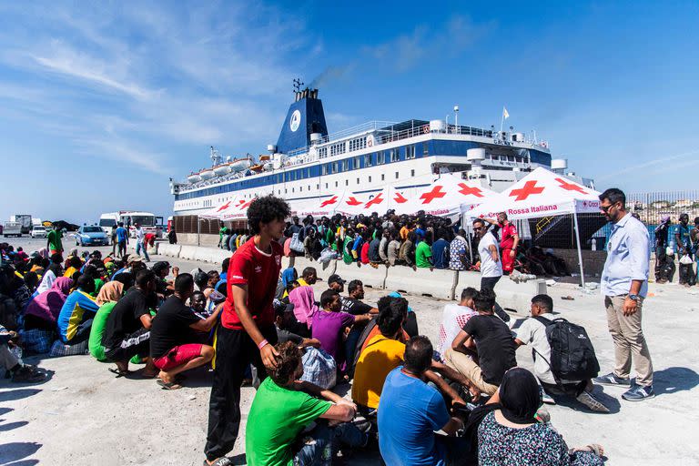 Migrantes de un centro de alojamiento para inmigrantes en la isla italiana de Lampedusa son guiados por un funcionario de seguridad el 14 de septiembre de 2023, mientras se preparan para abordar el barco 