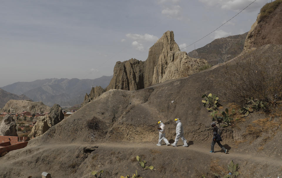 Vestidos en trajes de protección, doctores recorren un camino de tierra durante una campaña de testeo de coronavirus casa por casa en Avircato, Bolivia, el martes 7 de julio de 2020. (AP Foto/Juan Karita)