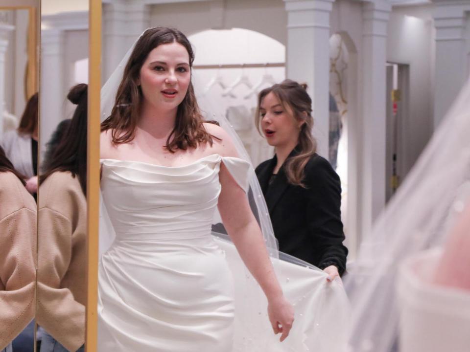 A woman looks at herself in a mirror as she wears a wedding dress.