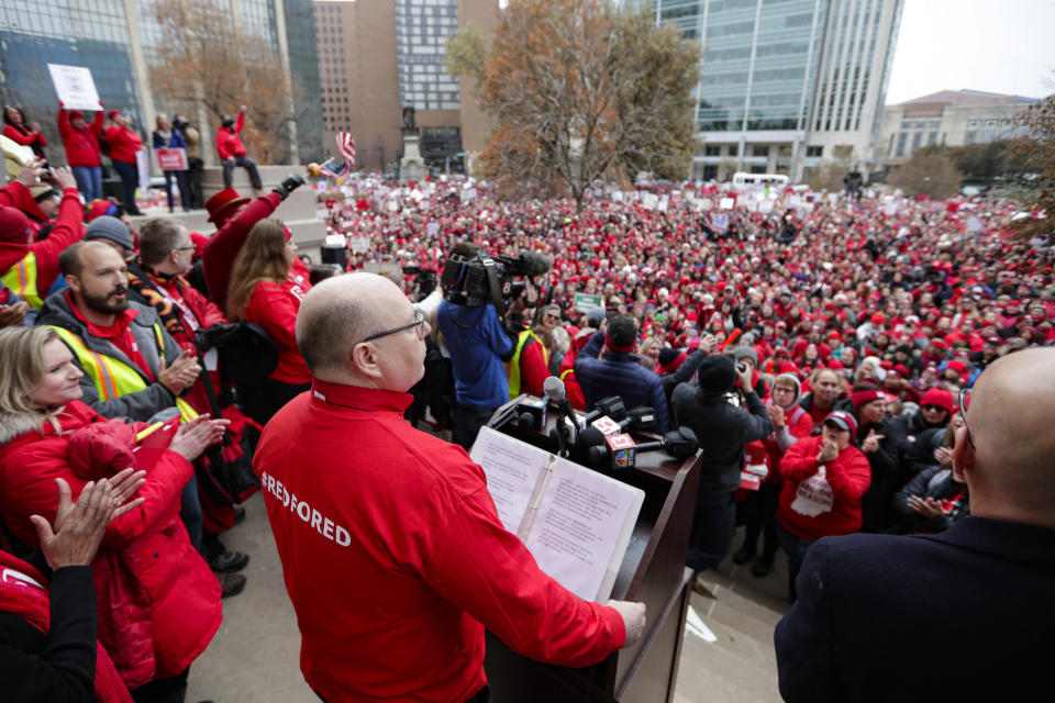 Keith Gambill, president of the Indiana State Teachers Association, of Evansville, Ind., speaks to the thousands of Indiana teachers wearing red as they surrounded the Statehouse in Indianapolis, Tuesday, Nov. 19, 2019 for a rally calling for further increasing teacher pay in the biggest such protest in the state amid a wave of educator activism across the country. Teacher unions says about half of Indiana's nearly 300 school districts are closed while their teachers attend Tuesday's rally while legislators gather for 2020 session organization meetings.(AP Photo/Michael Conroy)