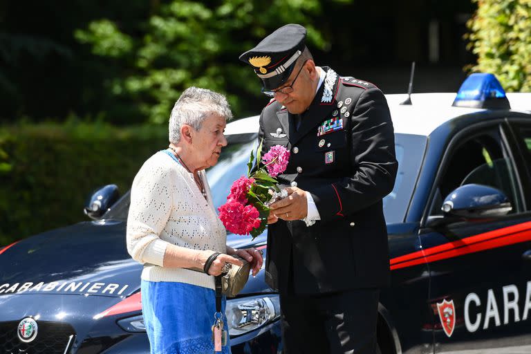 Un carabinero asiste a una mujer que se acercó a dejar una ofrenda de flores por Berlusconi