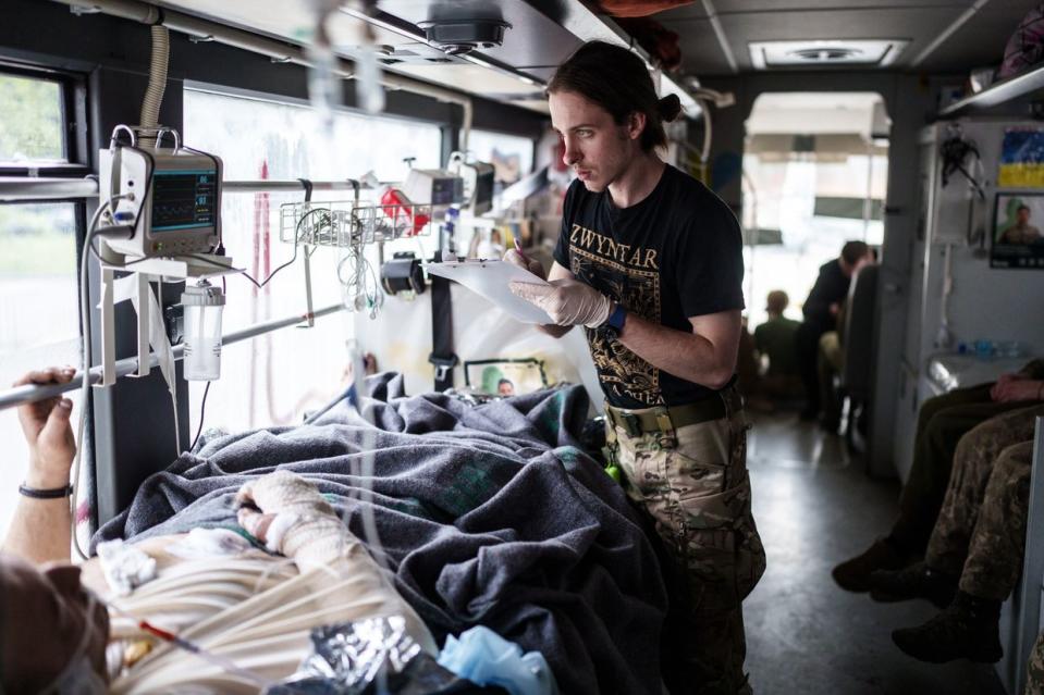 One of the volunteers with the Hospitallers Medical Battalion writes down the medical data of the wounded soldier inside the evacuation bus that brings wounded Ukrainian soldiers from Donetsk Oblast to a hospital in Dnipro city on April 25, 2024. (Serhii Korovayny/The Kyiv Independent)