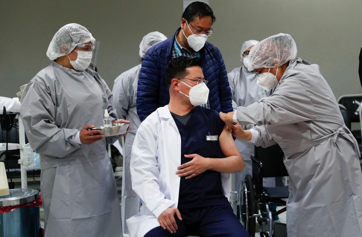 Bolivia's President Luis Arce, center back, watches as a healthcare worker vaccinates Dr. Rafael Rodriguez with a dose of Russia's Sputnik V COVID-19 vaccine, at the Del Norte Hospital in El Alto, Bolivia, Saturday, Jan. 30, 2021.