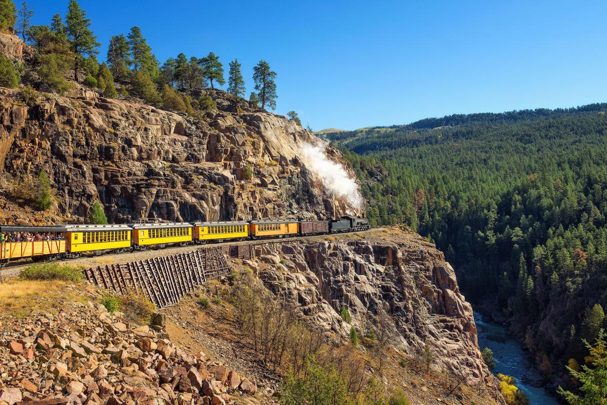 Historical steam engine train, with yellow railroad cars, in motion through the San Juan Mountains, Colorado on a bright sunny day in summer
