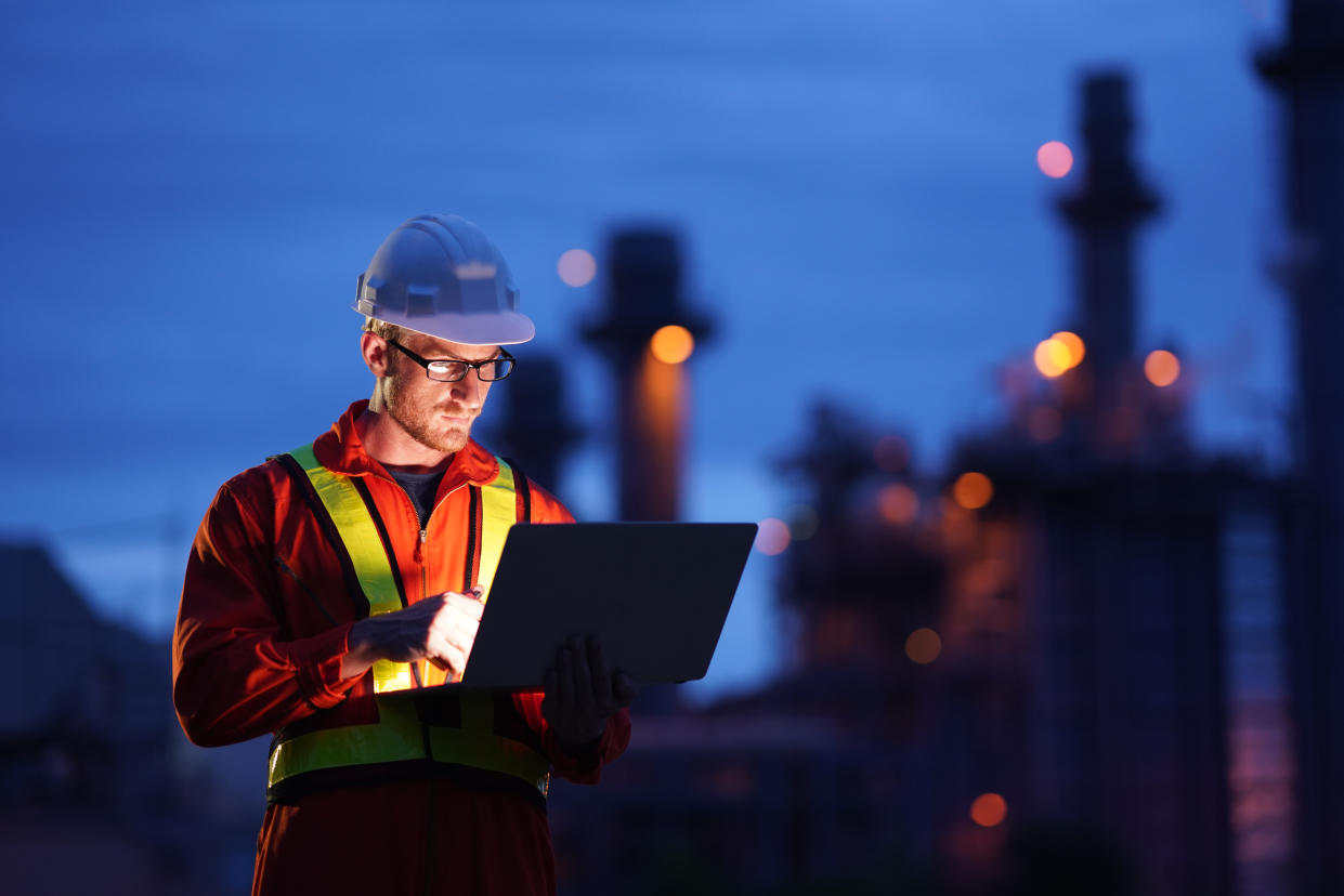 Engineer using laptop working while standing over Natural gas power Plant at construction site in evening twilling