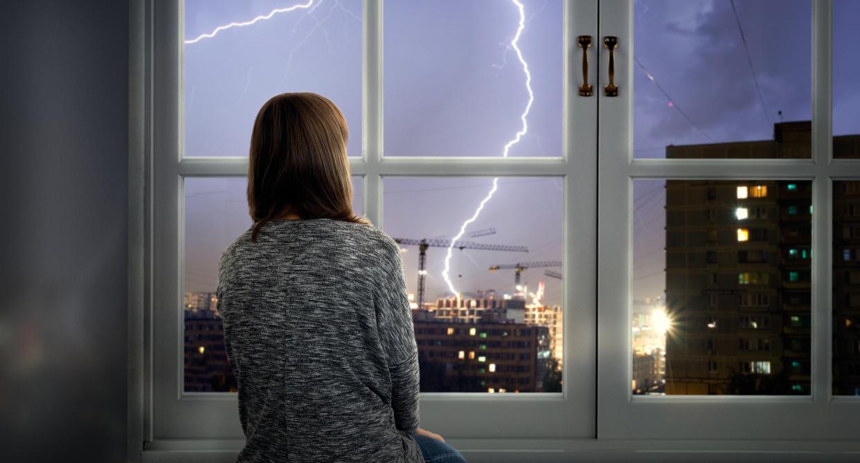 Woman looks out window during thunderstorm, but are thunderstorm headaches a real thing?
