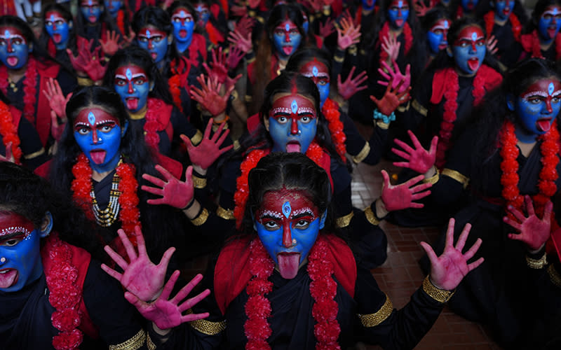 Students at a college with faces painted in blue and hands painted red pose with their tongues out for the media at an event held