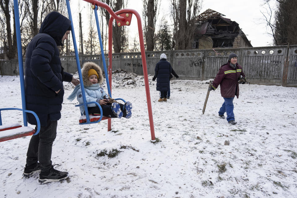 A man pushes his daughter on a swing in front of a tax office building that was heavily damaged by a Russian attack in Kyiv, Ukraine, Wednesday, Dec. 14, 2022. (AP Photo/Evgeniy Maloletka)