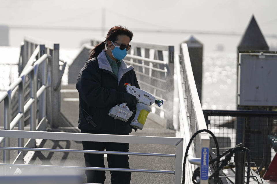 A woman disinfects the handrails of the main dock gangway on Alcatraz Island in San Francisco, Monday, March 15, 2021. The historic island prison was reopened to visitors Monday after being closed since December because of the coronavirus threat. Visitors were also able to tour the inside of the main cell house for the first time in a year. (AP Photo/Eric Risberg)