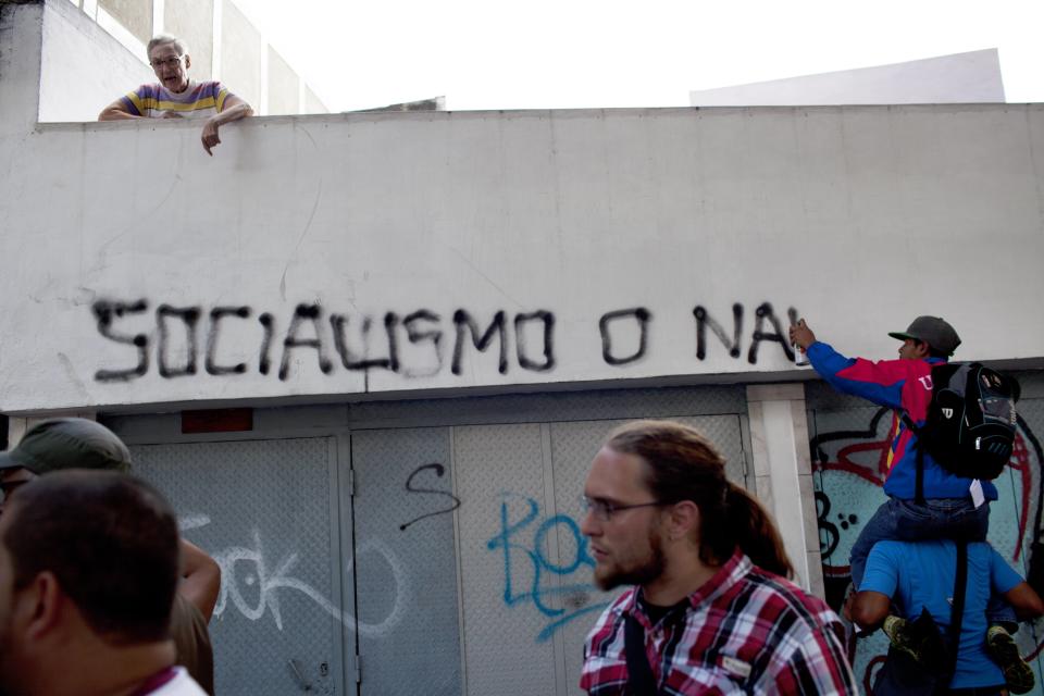 A woman yells at members of a pro-government "colectivo," or "collective," writing graffiti on her home that reads in Spanish "Socialism or nothing" in downtown Caracas, Venezuela, Thursday, Feb. 20, 2014. President Nicolas Maduro and his supporters say the escalating protests against his socialist government in the oil-rich but economically struggling country are part of an attempted coup sponsored by right-wing and "fascist" opponents in Venezuela and abroad, particularly the United States. (AP Photo/Rodrigo Abd)