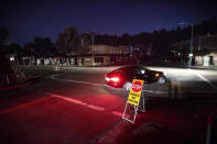 A car drives through a darkened Montclair Village as Pacific Gas & Electric power shutdowns continue in Oakland, Calif. The area remains without power after the utility cut service hoping to prevent wildfires during dry, windy conditions. (AP Photo/Noah Berger)