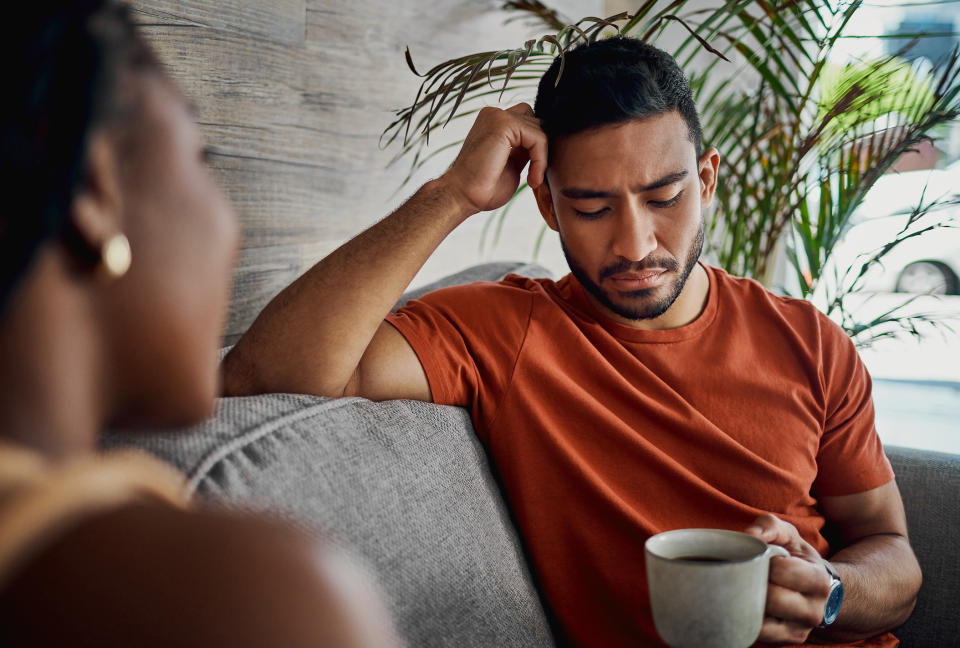 Man sitting on a couch and looking sad as he holds a cup of coffee