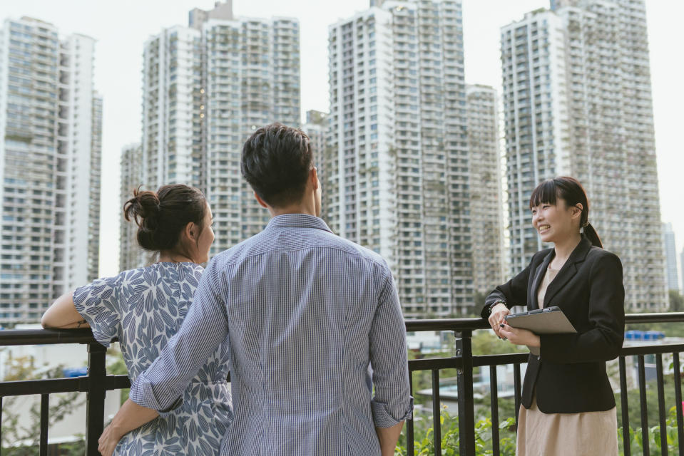 Back view of an Asian couple looking to buy a new home, possibly a HDB flat, in a meeting with a real estate agent.