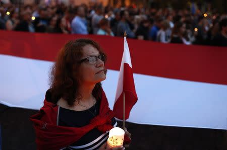 A woman holds a candle as she stands next to a Polish flag during a protest against supreme court legislation in Warsaw, Poland, July 21, 2017. REUTERS/Kacper Pempel