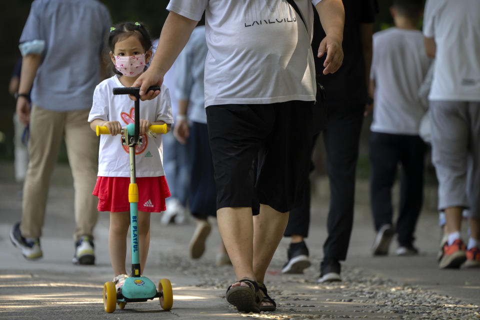 A child wearing a face mask rides a scooter along a path at a public park in Beijing, Tuesday, Aug. 30, 2022. (AP Photo/Mark Schiefelbein)