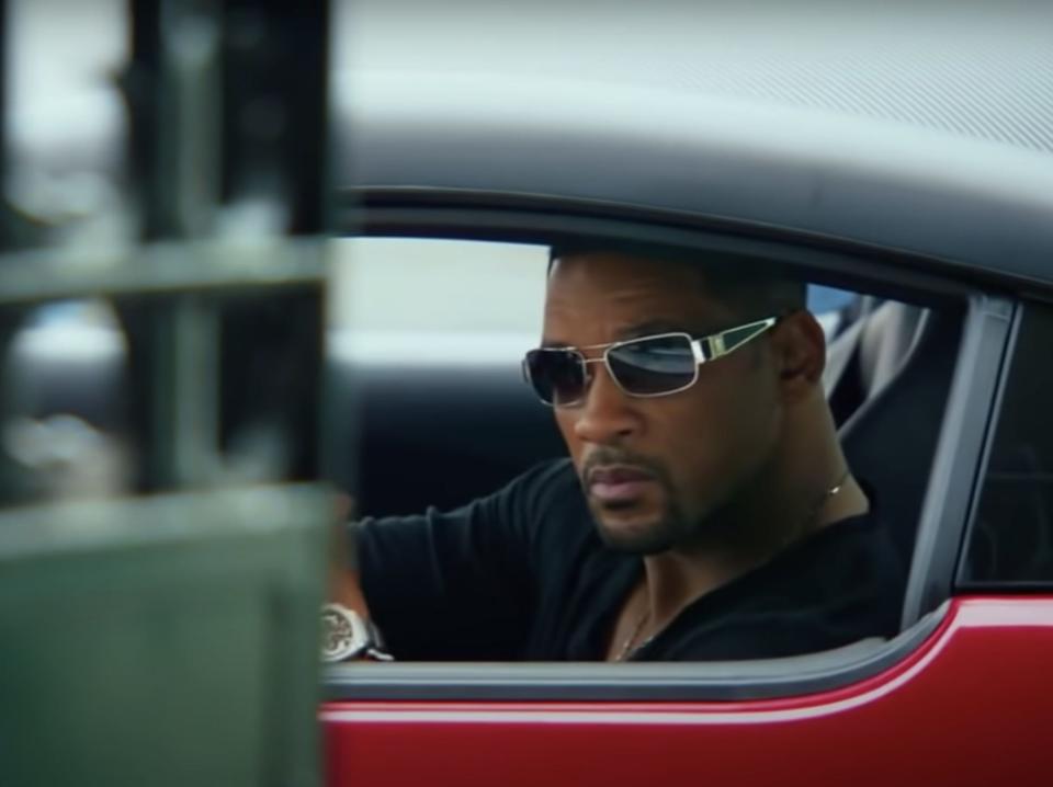 Will Smith wearing sunglasses in a red car in focus