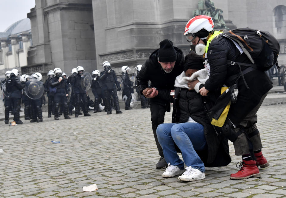 Two people help a woman overcome by tear gas during a demonstration against COVID-19 measures in Brussels, Sunday, Jan. 23, 2022. Demonstrators gathered in the Belgian capital to protest what they regard as overly extreme measures by the government to fight the COVID-19 pandemic, including a vaccine pass regulating access to certain places and activities and possible compulsory vaccines. (AP Photo/Geert Vanden Wijngaert)