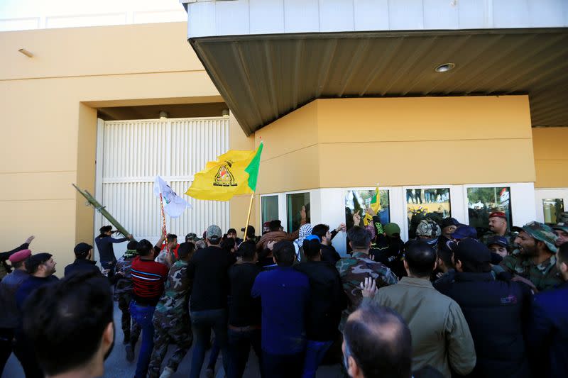 Protesters and militia fighters gather to condemn air strikes on bases belonging to Hashd al-Shaabi, outside the main gate of the U.S. Embassy in Baghdad