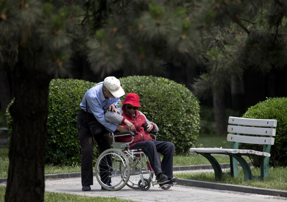 In this Thursday, May 23, 2013 photo, an elderly man helps his wife on a wheelchair at a park in Beijing. New wording in the law requiring people to visit or keep in touch with their elderly parents or risk being sued came into force Monday, as China faces increasing difficulty in caring for its aging population. (AP Photo/Andy Wong)