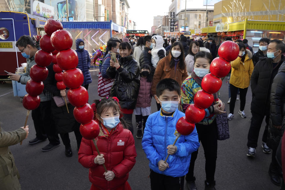 Young children wearing masks to protect from the coronavirus pose for photos with giant replica of candy haw, a popular Beijing snack, at a street stall near Wangfujing on the fourth day of the Lunar Chinese New Year in Beijing on Monday, Feb. 15, 2021. (AP Photo/Ng Han Guan)