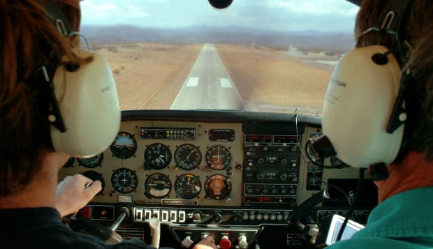 2 pilots landing a a small single engine airplane. The runway is seen out the windscreen.