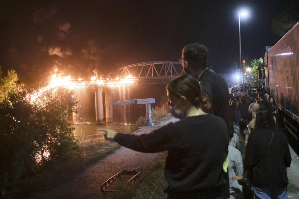 People look at flames engulfing the Industry Bridge in Rome, early Sunday, Oct. 3, 2021. A blaze, possibly sparked by a gas canister explosion, destroyed part of an historic bridge spanning the Tiber River in Rome before firefighters extinguished the flames early Sunday. (Mauro Scrobogna/LaPresse via AP)