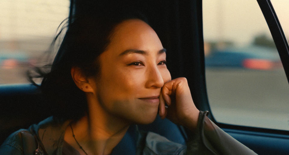 Greta Lee as Norah, smiling in the back of a cab on her way to New York City, in "Past Lives" 