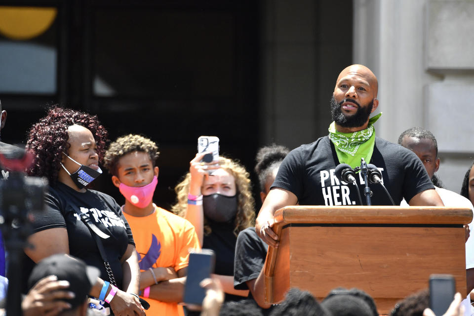 As Tamika Palmer, left, the mother of Breonna Taylor looks on, the artist Common addresses the crowd gathered on the steps of at the Kentucky State Capitol in Frankfort, Ky., Thursday, June 25, 2020. The rally was held to demand justice in the death of Taylor who was killed in her apartment by members of the Louisville Metro Police Department on March 13, 2020. (AP Photo/Timothy D. Easley)