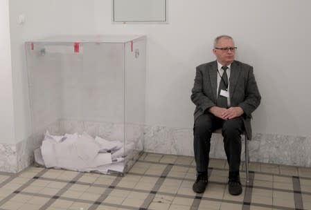 A member of the electoral commission sits near the ballot box during parliamentary election at a polling station in Warsaw