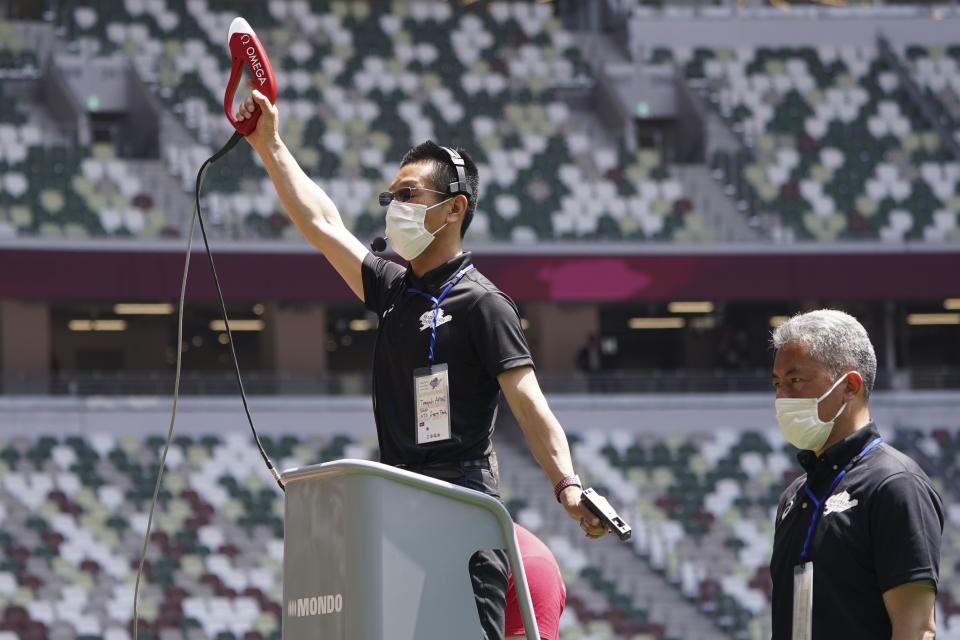 An official wearing a face mask uses a starter pistol to signal the start a women's 100 meter heat at an athletics test event for the Tokyo 2020 Olympics Games at National Stadium in Tokyo, Sunday, May 9, 2021. The competition entitled: "Ready Steady Tokyo - Athletics." (AP Photo/Shuji Kajiyama)