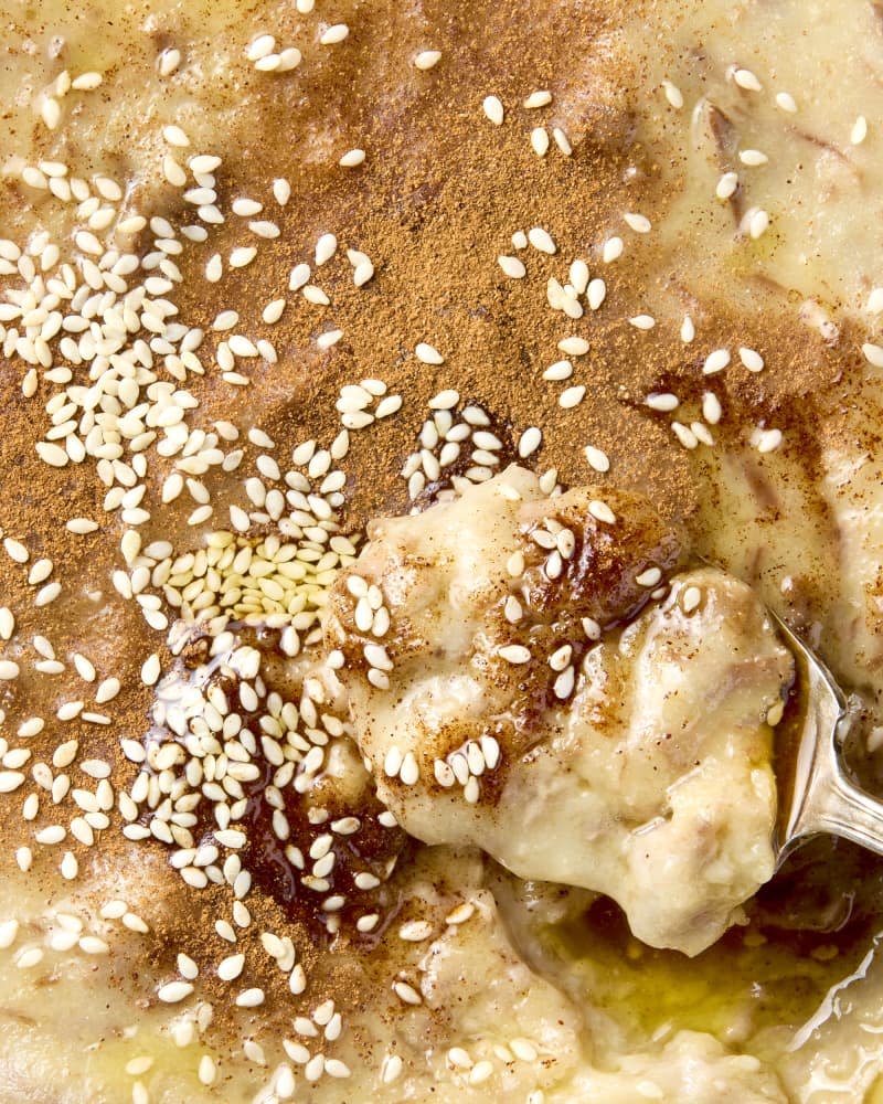 overhead shot of haleem in a white bowl, topped with cinnamon and sesame seeds.