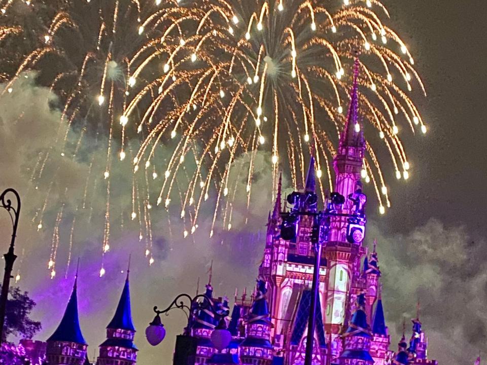 Image of fireworks at the Magic Kingdom at Disney. The castle is lit by purple lights and the fireworks are gold.