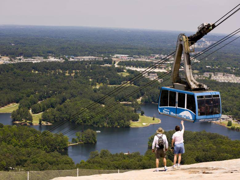 FILE - Two guests at Stone Mountain Park in Stone Mountain, Ga. wave at the Skyride as it brings more guests down to the ground from the mountain. The park was ranked as one of the best in Georgia by Tripadvisor.