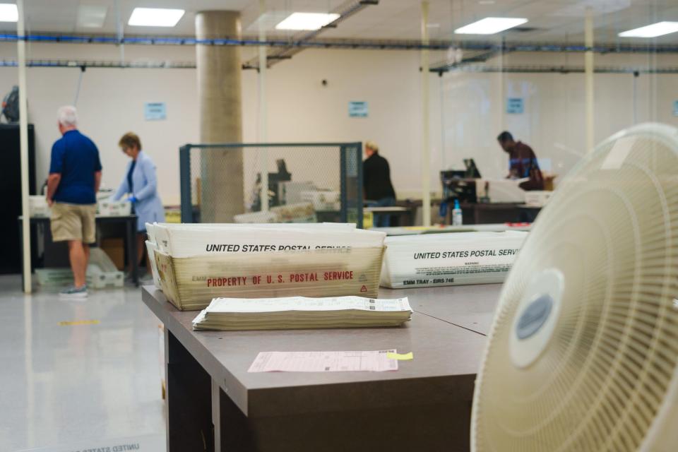 United States Postal Service bins and a stack of ballots sit on a table as early voter mail-in ballots are counted at the Maricopa County Tabulation and Election Center on Aug. 1, 2022, in Phoenix, Ariz.