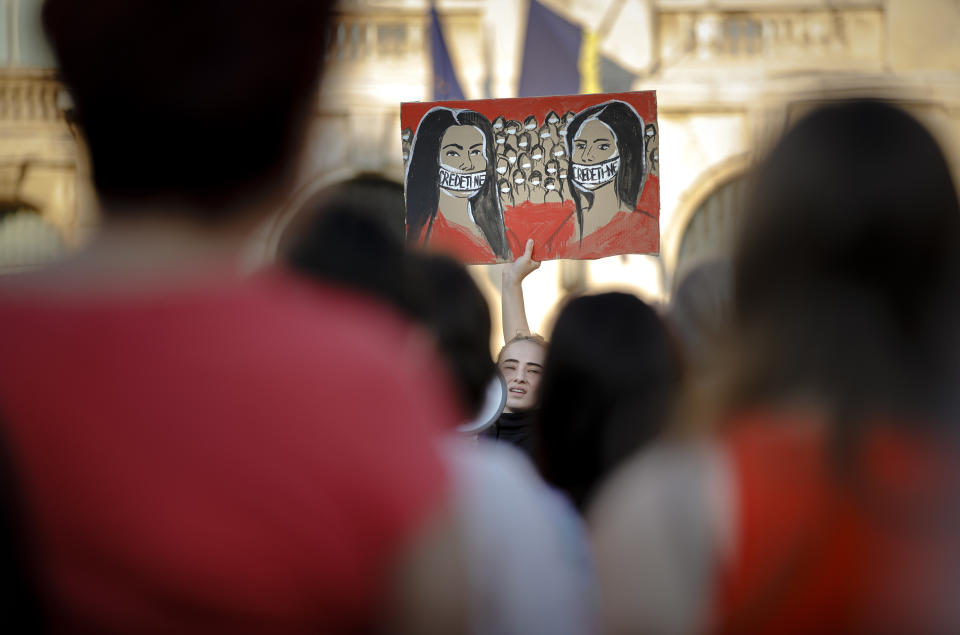 A protester holds a placard depicting women their mouth covered by tape that reads "Believe us" during a rally in memory of a 15 year-old girl, raped an killed in southern Romania, after police took 19 hours from the moment she called the country's emergency hotline to intervene, in Bucharest, Romania, Sunday, July 28, 2019. More than one hundred people took part Sunday evening in a protest against the way police handled the case. (AP Photo/Vadim Ghirda)