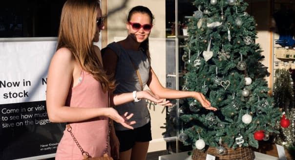 young females wearing summer clothes on hot sunny day bemused at early christmas shop window display