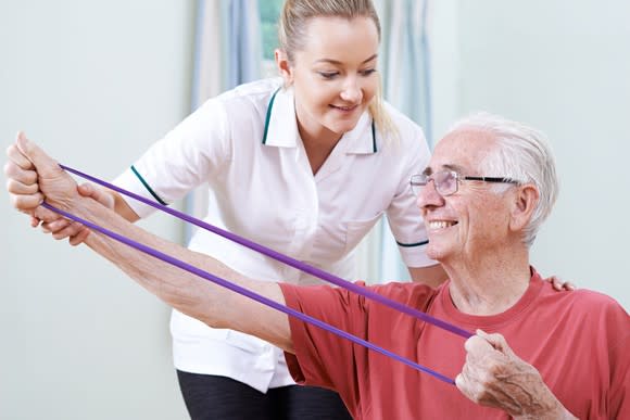 A smiling older man works with a physical therapist.