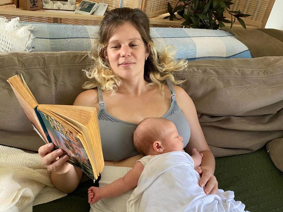 Mother reading a book on coach with baby laying on her.