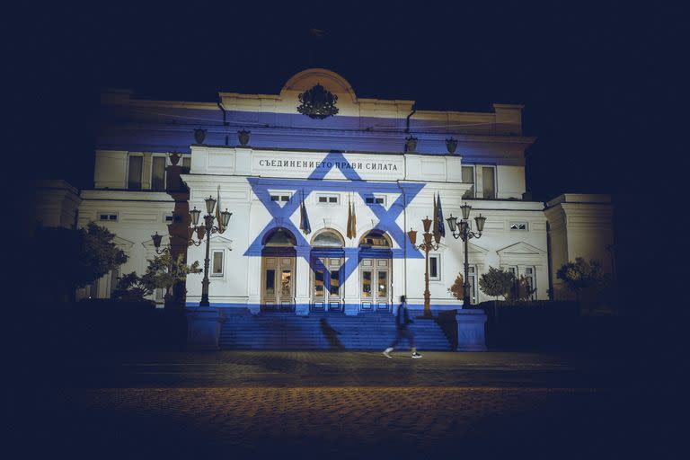 Una persona pasa frente a la bandera de Israel, que está proyectada en el edificio del Parlamento búlgaro, en Sofía, Bulgaria, el domingo 8 de octubre de 2023, para mostrar su apoyo a Israel tras la invasión sin precedentes de Hamás desde Gaza. (Foto AP/Valentina Petrova)