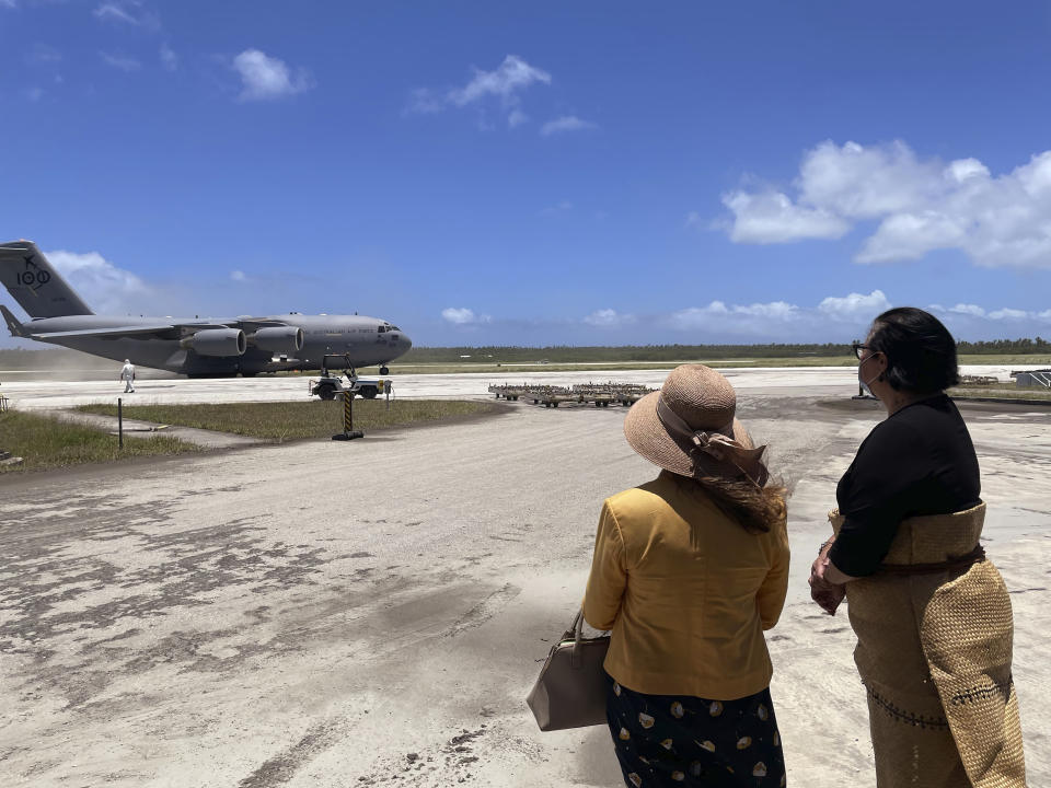 In this photo provided by the Australian Defence Force, the Tongan Foreign Minister, Fekitamoeloa 'Utoikamanu, right, and the Australian High Commissioner to Tonga, Rachael Moore, watch the arrival of the first Royal Australian Air Force C-17A Globemaster III aircraft at Fua'amotu International Airport near Nukuʻalofa, Tonga, Thursday, Jan. 20, 2022. The first flights carrying fresh water and other aid to Tonga were finally able to land after the Pacific nation's main airport runway was cleared of ash left by a huge volcanic eruption. (Australian Defence Force via AP)