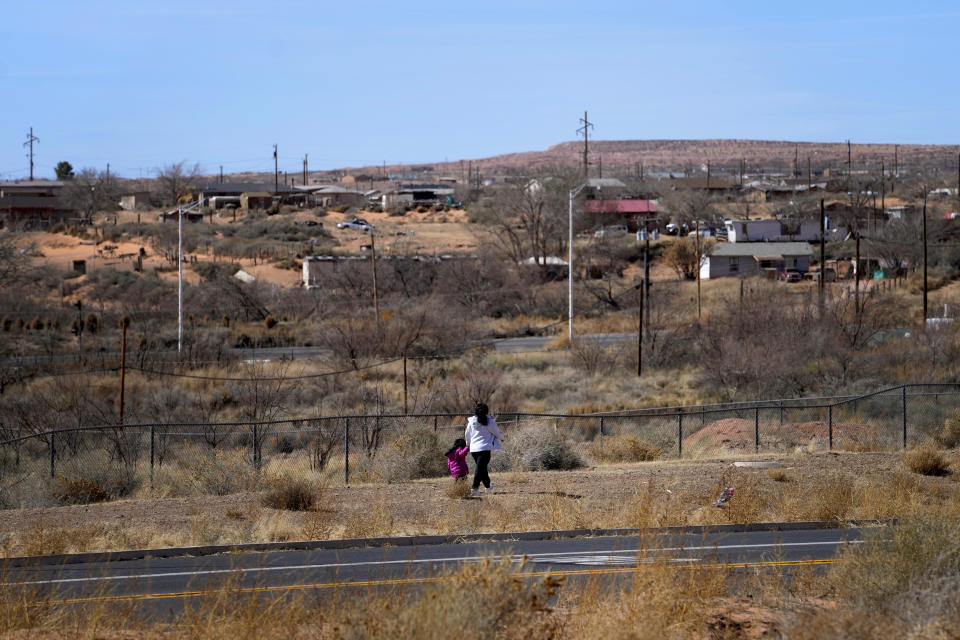 People walk on the Hopi reservation toward the Navajo Nation, top, just yards from U.S. 160, Monday, March 4, 2024, in Tuba City, Ariz. The highway is the de facto border between the Navajo and Hopi Indian reservations and two time zones. Mind-bending time calculations is what people in the largest Native American reservation in the U.S. have to endure every March through November. (AP Photo/Matt York)