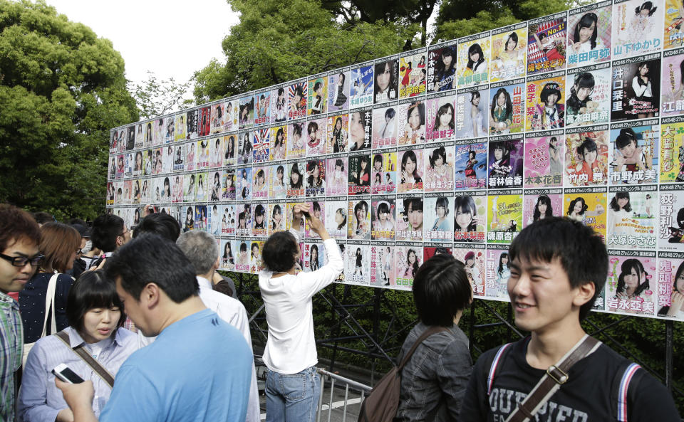 FILE - In this June 6, 2012 file photo, fans of Japan’s all-girl pop idol group AKB48 take photos of the members' election posters outside the venue of the annual AKB48 popularity poll in Tokyo. More than 60 girls and young women, split into four teams, make up what is arguably Japan's most popular pop group. It performs almost every day, has spawned affiliate groups across the country and has recently given rise to sister mega-groups in China and Indonesia. (AP Photo/Shizuo Kambayashi, File)